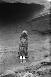a woman in a fur coat standing in front of a cave