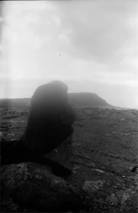 a black and white photo of a person sitting on a rock